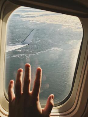 A hand on an airplane window overlooking a city