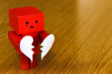 A red wooden figure holding a broken heart