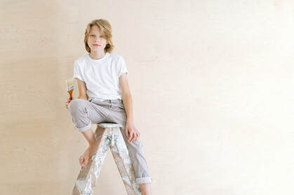 A boy sitting on a ladder with a paintbrush in his hand.