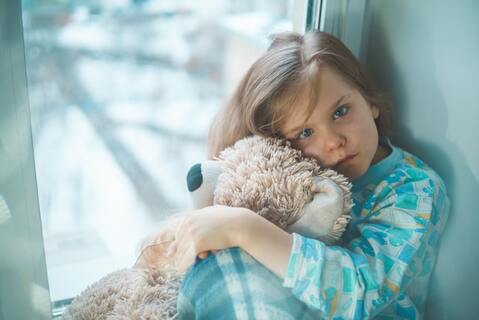 A sad girl hugging a teddy bear
