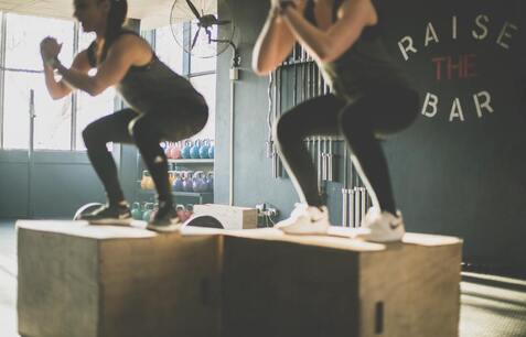 Two people squat on elevated blocks in a fitness class.
