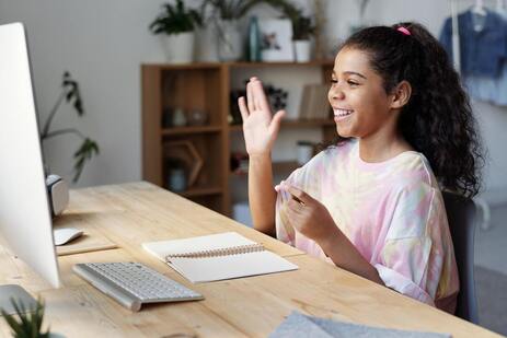 A girl waving at a computer screen and smiling